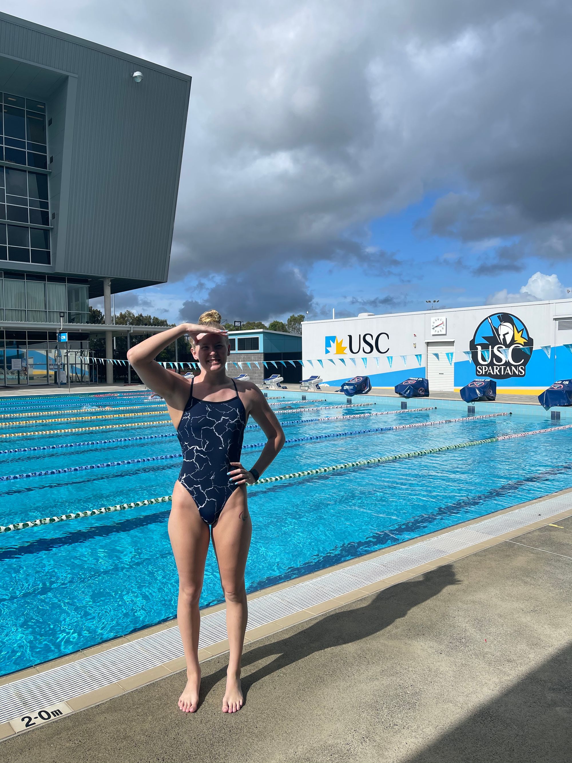 athlete standing on pool deck shading her eyes from the sun with her hand