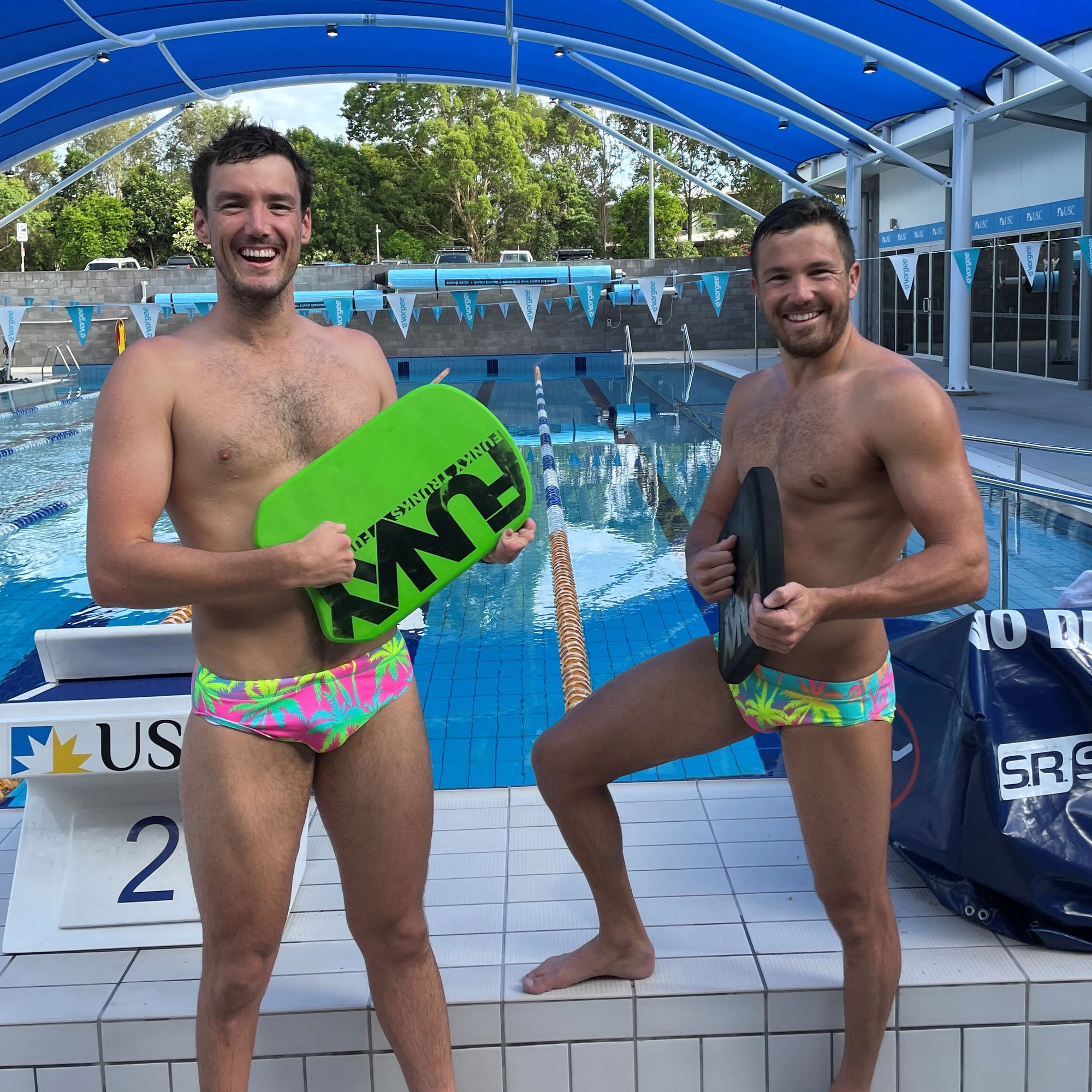 two swimmers on pool deck holding kick boards