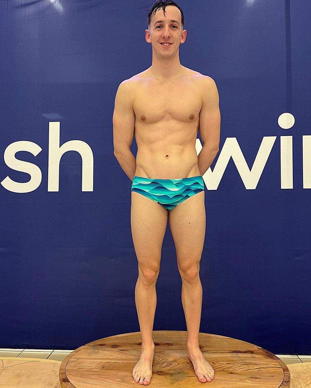 swimmer standing on podium with bathers on and hands behind his back